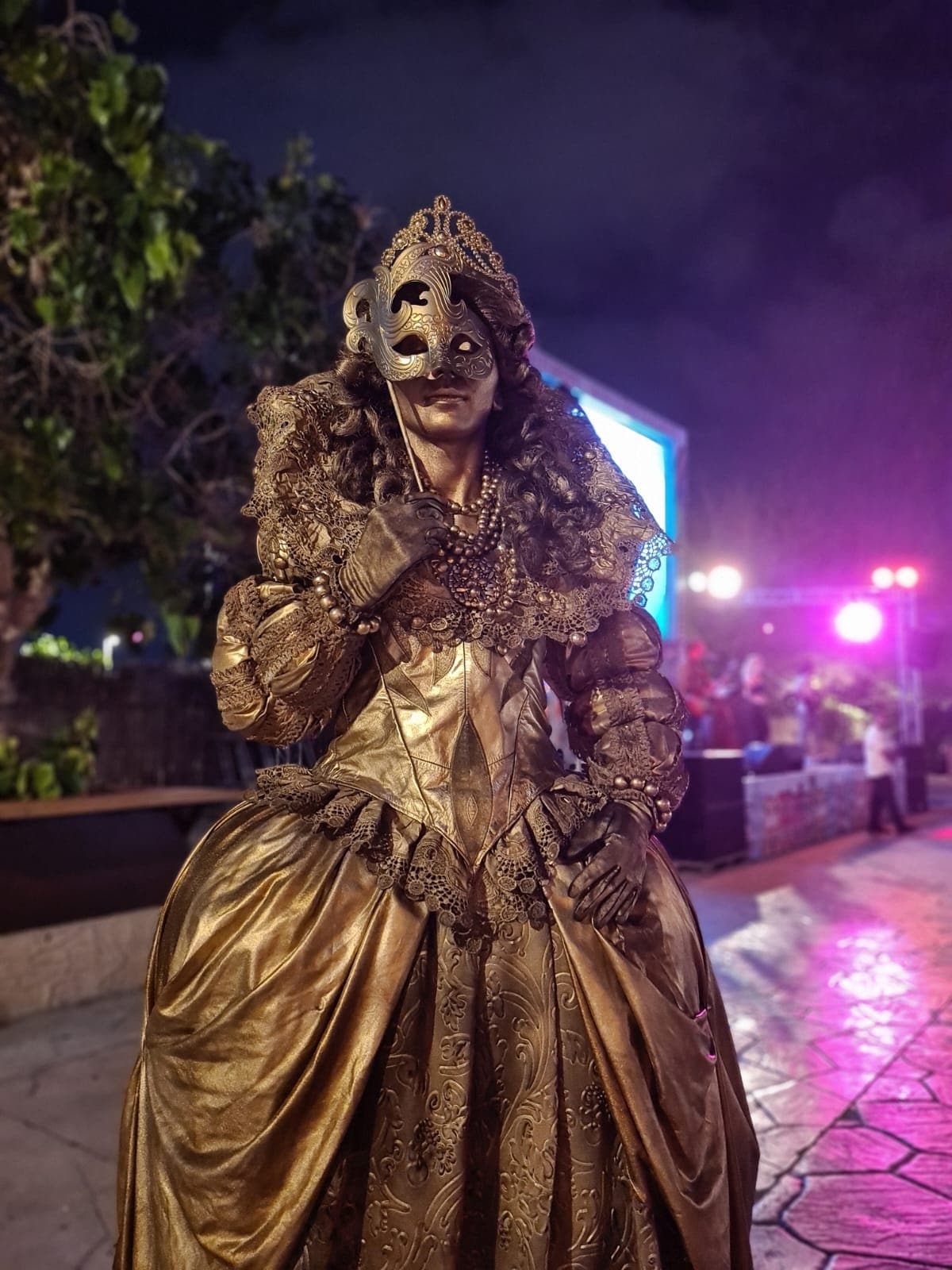 Gold-painted living statue performer in an ornate masquerade gown and mask