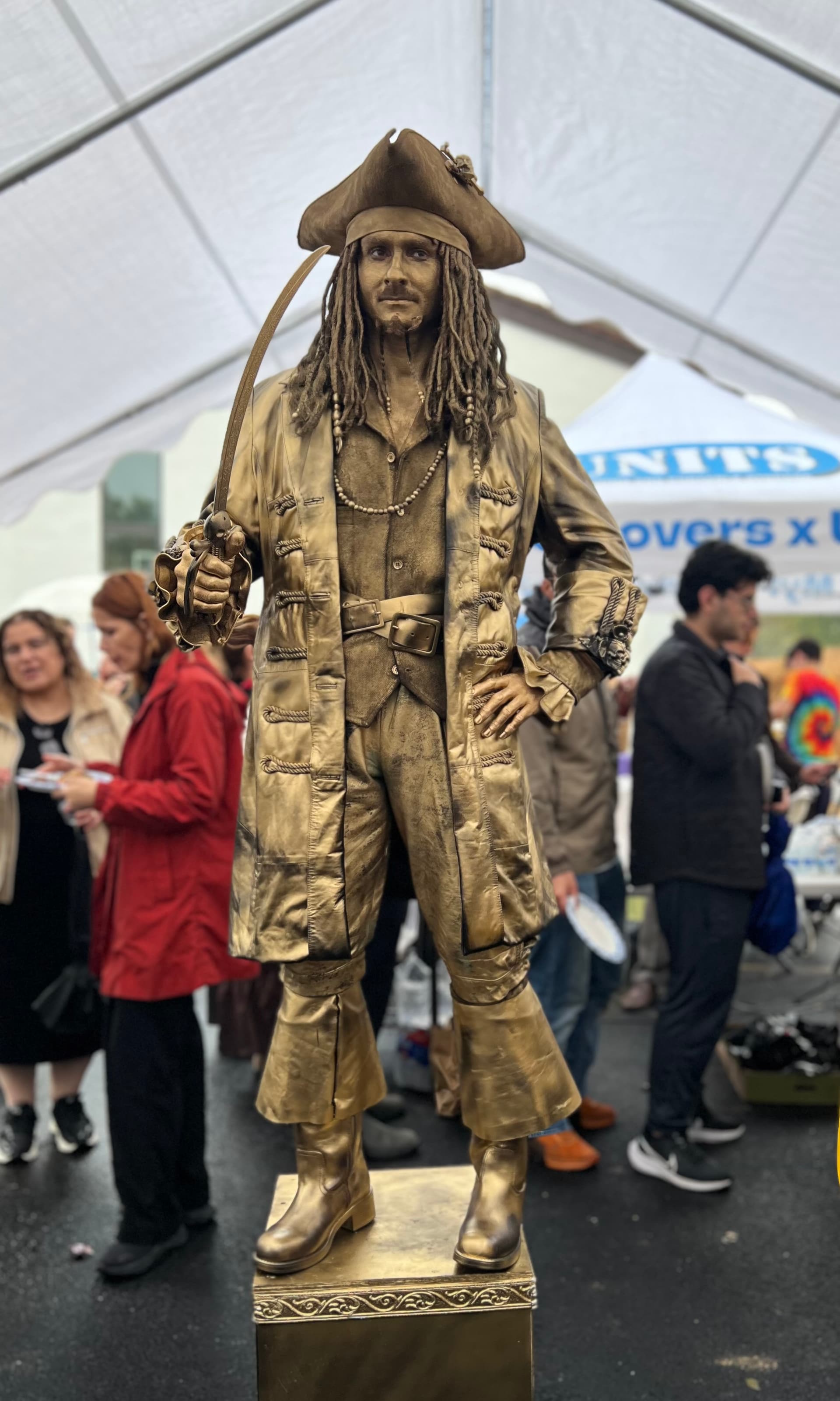 Gold-painted pirate living statue on a pedestal at an outdoor festival