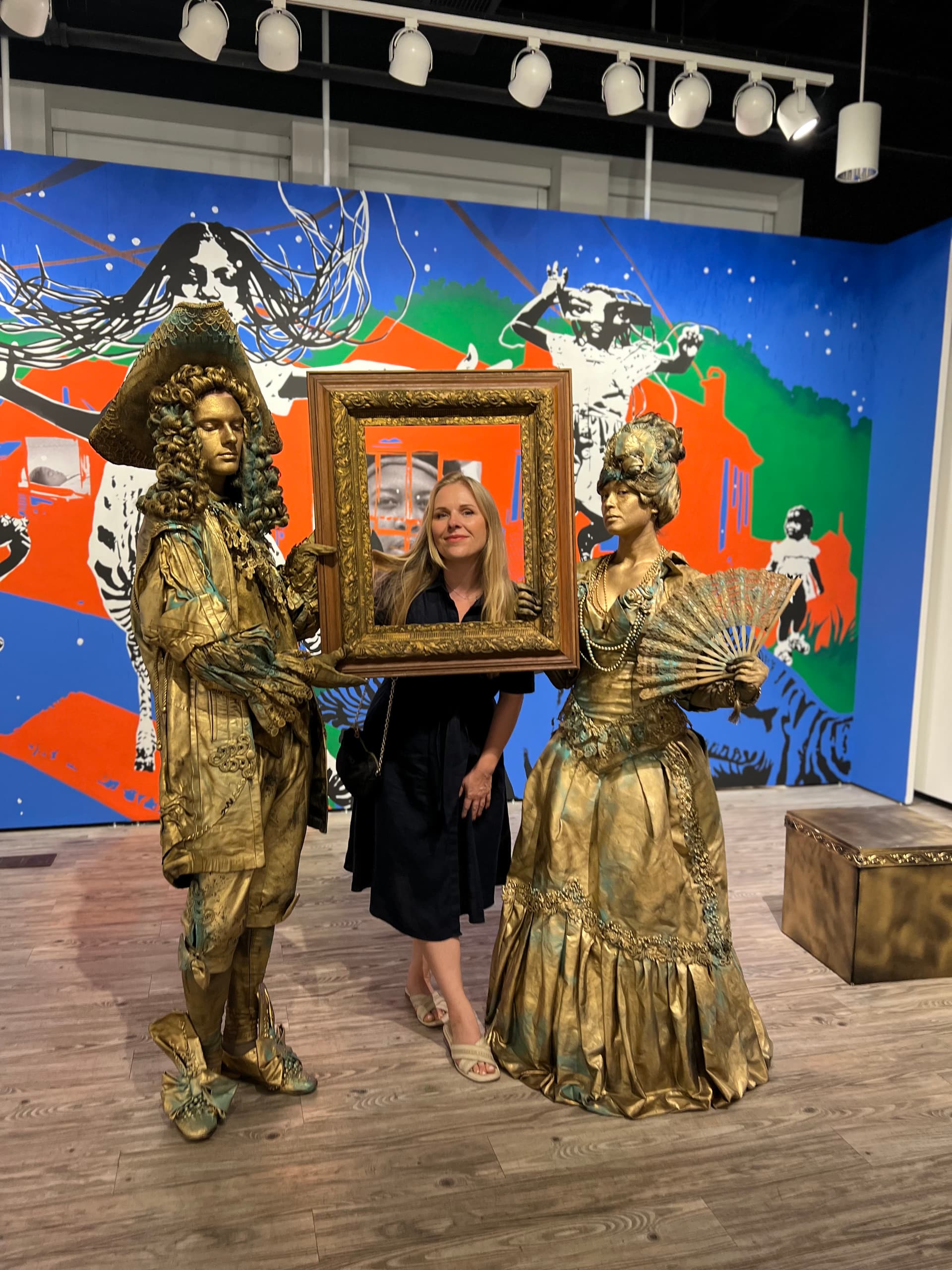 Guest posing with an ornate gold frame between two gold baroque living statues
